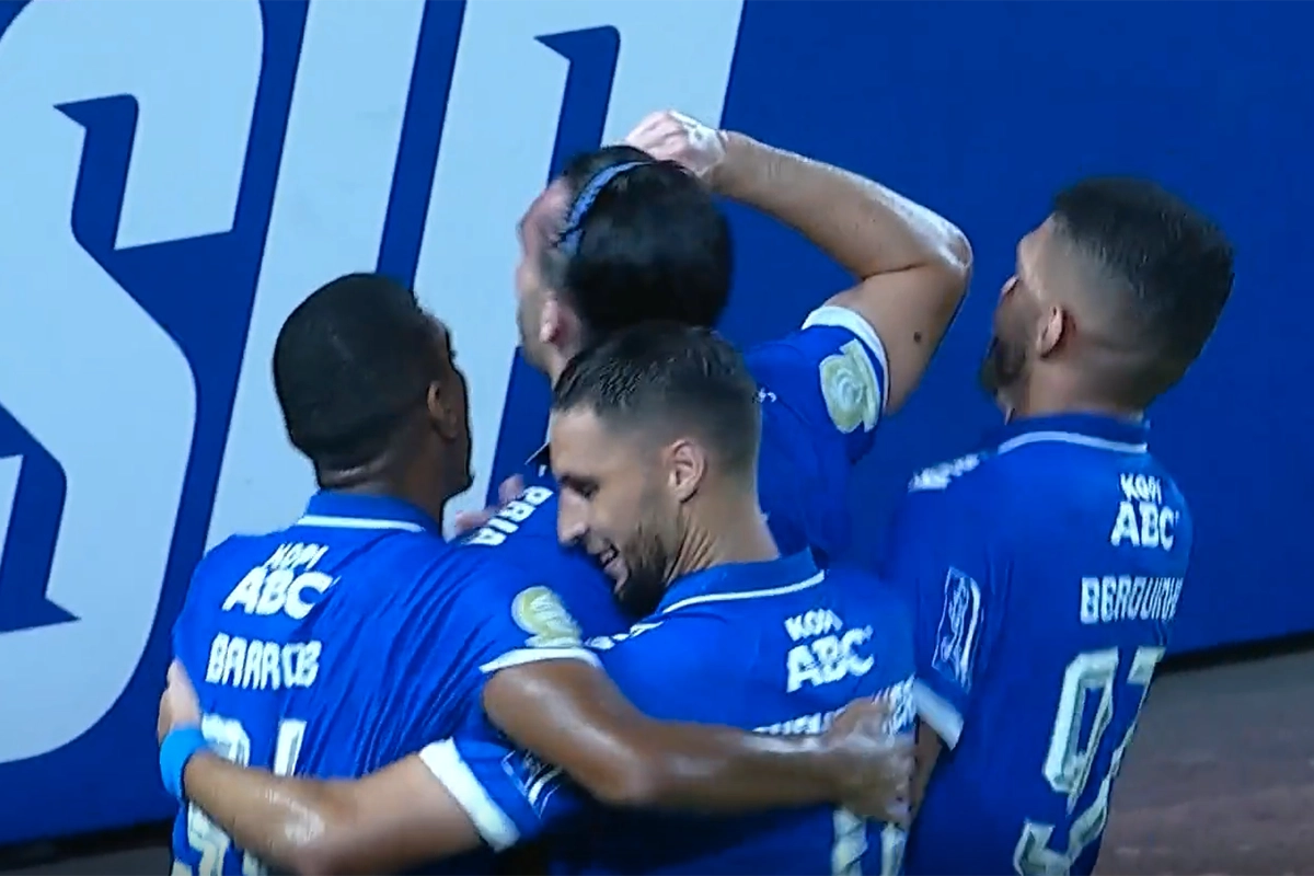 Pemain Persib Bandung, termasuk Ciro Alves dan David da Silva, berpelukan merayakan gol di depan papan iklan bertuliskan "PERSIB" di stadion.