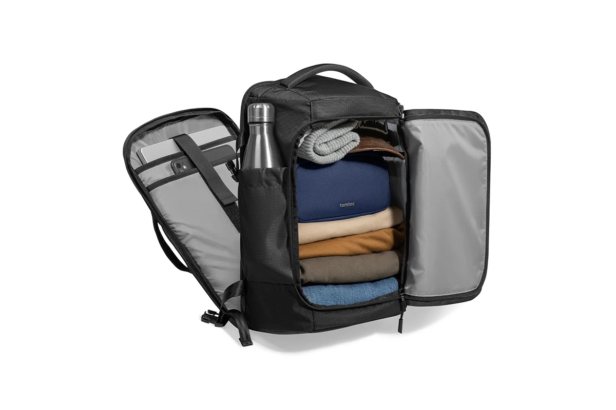 Tampilan interior tas Tomtoc Navigator T66 40L yang terbuka lebar (clamshell) berisi tumpukan pakaian, packing cube, botol minum di saku samping, dan laptop di kompartemen belakang.