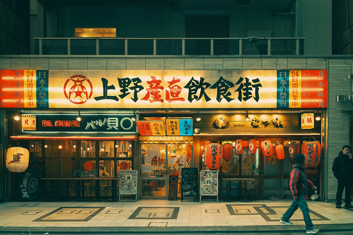 Pemandangan jalan di Jepang pada malam hari dengan restoran berhias lampion merah dan papan nama menyala, ilustrasi lingkungan sosial di mana turis harus menjaga etika.